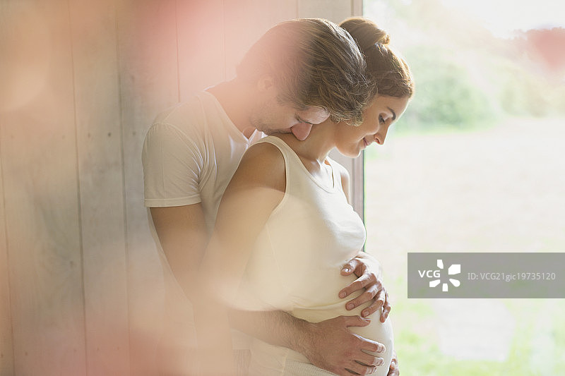 一对深情的怀孕夫妇在窗口拥抱图片素材