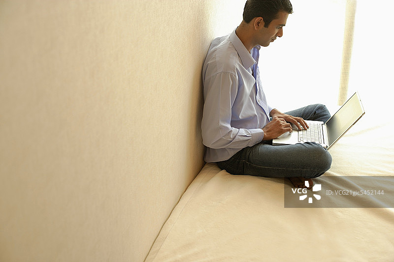 男子盘腿坐在床上，使用笔记本电脑图片素材