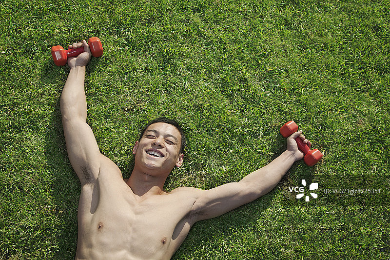 赤裸上身的男子躺在草地上，举着哑铃图片素材