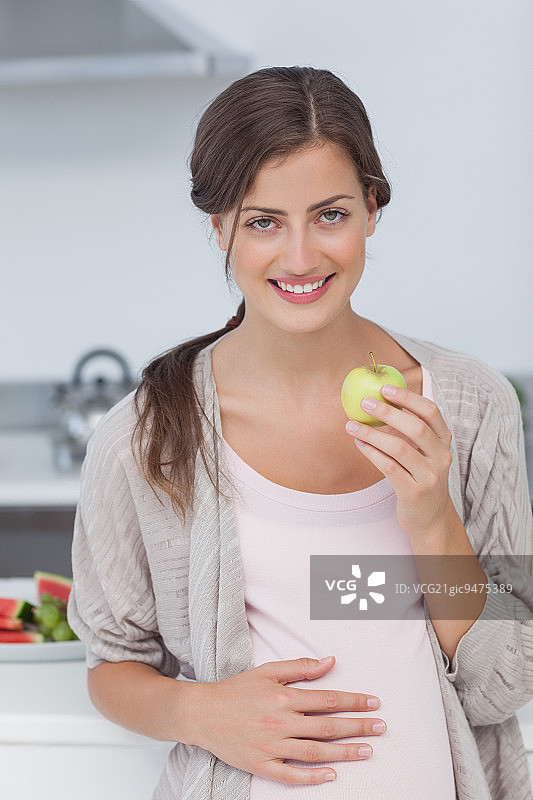 一个孕妇在厨房里拿着一个青苹果图片素材