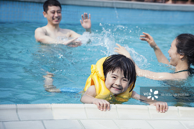微笑的儿子在水里的肖像，抱着池边和家人在背景图片素材