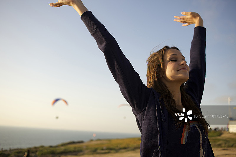 一位20岁出头的女性在加州的一个滑翔伞港口举起双臂，闭上眼睛感受风。图片素材