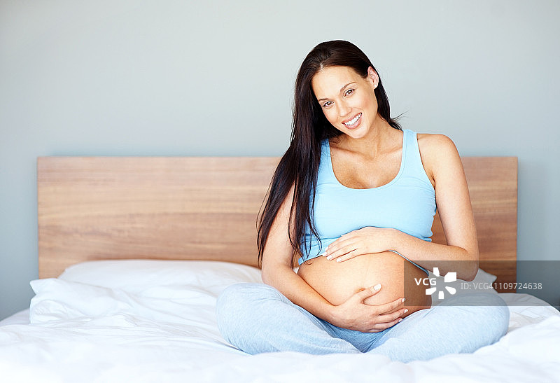 微笑的年轻孕妇坐在床上图片素材
