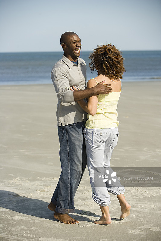 一对年轻夫妇在海滩上拥抱嬉戏图片素材