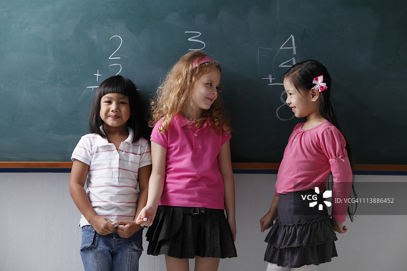三个年轻的女孩站在黑板前，互相微笑着图片素材
