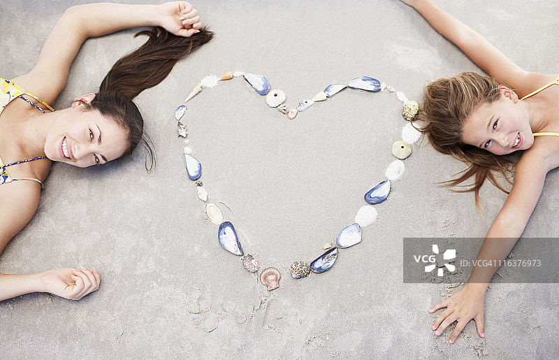 妈妈和女儿在沙滩上用贝壳形成的心图片素材