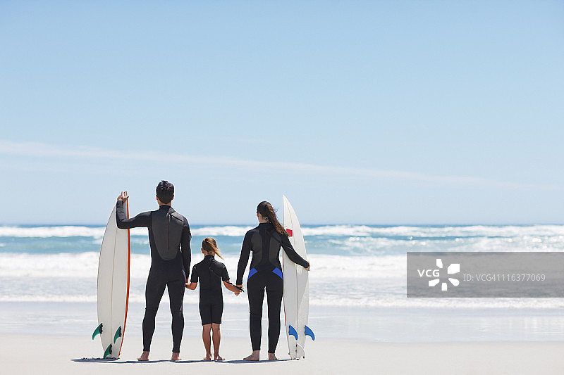 一家人穿着潜水衣手牵着手在沙滩上冲浪图片素材