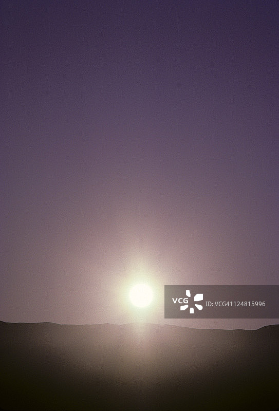 明亮耀眼的太阳球沉在山顶下，紫色的天空。图片素材