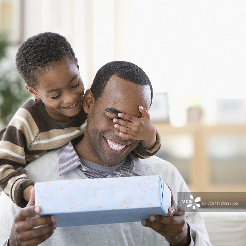 一个非裔美国男孩捂住父亲的眼睛，给他一份礼物图片素材