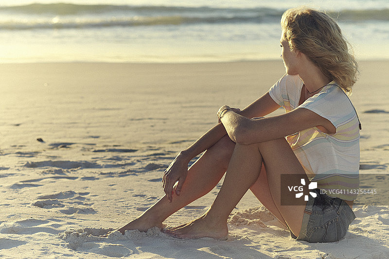 一个年轻女子坐在海滩上看海图片素材