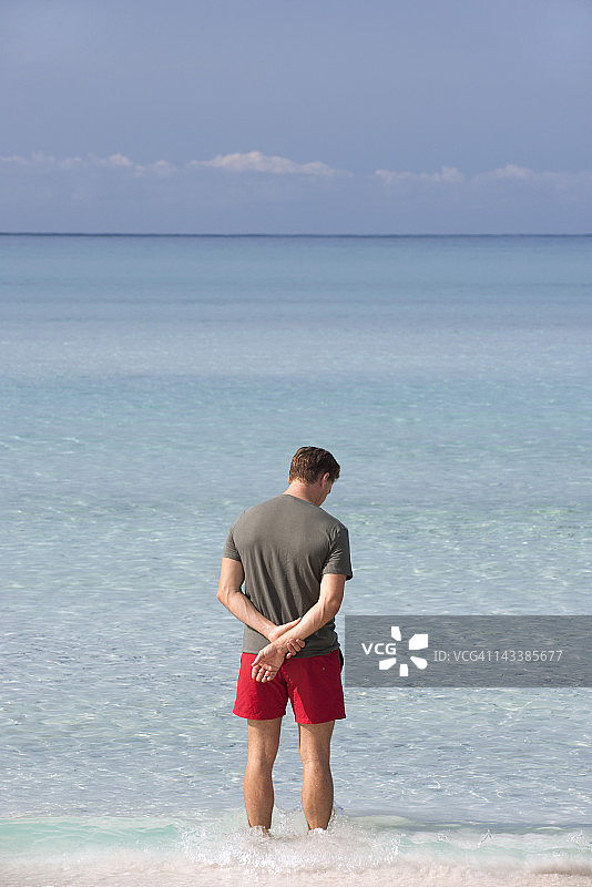 一名男子站在齐踝深的水中凝望大海，后视镜图片素材