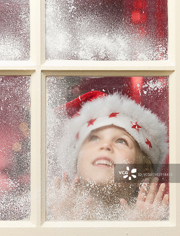 快乐的女孩透过下雪的窗户在圣诞节图片素材