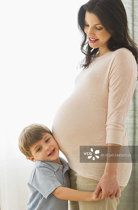 美国，新泽西州，泽西城，男孩(4-5)把耳朵贴在怀孕母亲的肚子上图片素材