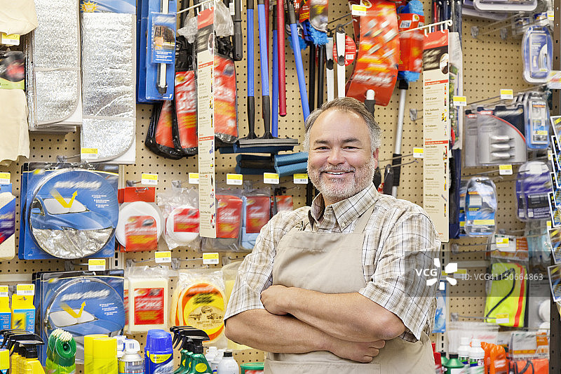 一个快乐的成熟的销售员双臂交叉在五金店的肖像图片素材