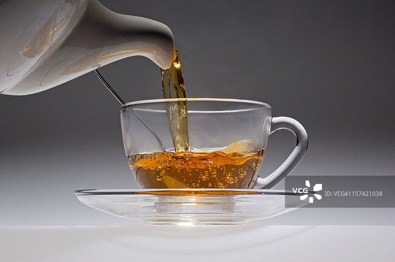 茶水从白色瓷壶倒入玻璃杯中。图片素材
