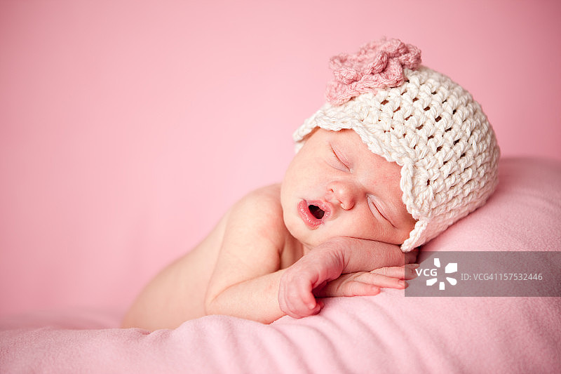 熟睡中的新生女婴戴着一顶粉红色的钩针帽子图片素材