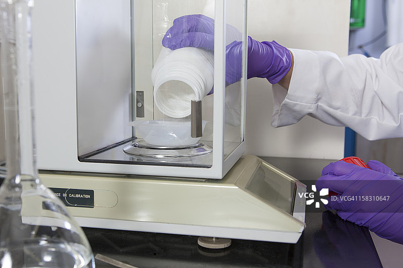 实验室科学家将固体试剂添加到一个容器中图片素材