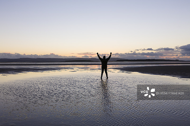 一个人举着胳膊站在海滩的水里图片素材