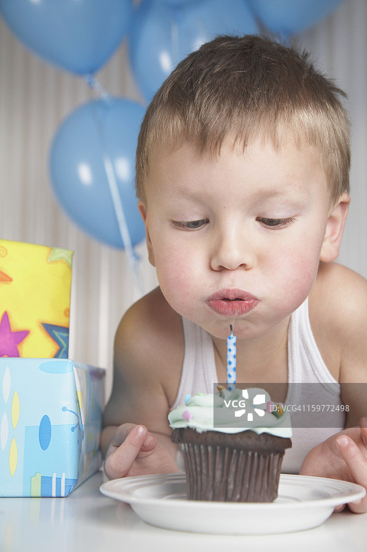 小男孩吹灭纸杯蛋糕上的蜡烛。图片素材