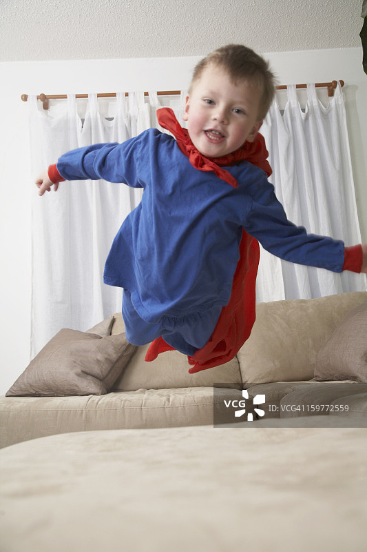 小男孩打扮成超级英雄在沙发上跳。图片素材