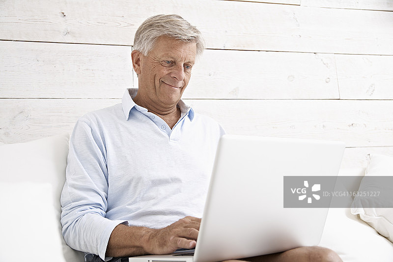 西班牙，老男人在笔记本电脑上查看邮件，面带微笑图片素材