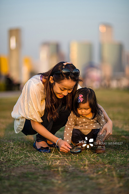 漂亮的妈妈和孩子使用放大镜在草地上图片素材