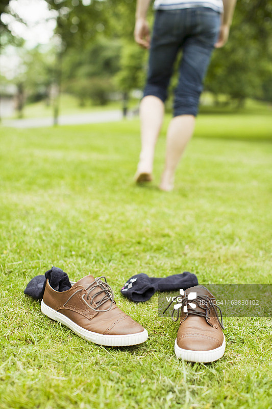 在草地上穿着袜子和鞋子，后面是在公园里走路的男人图片素材