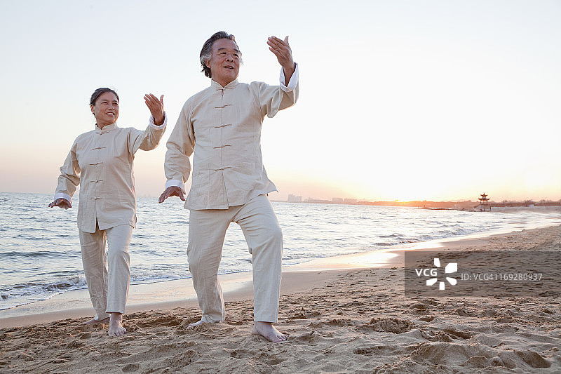 中国，日落时分，两个老人在海滩上练习太极拳图片素材