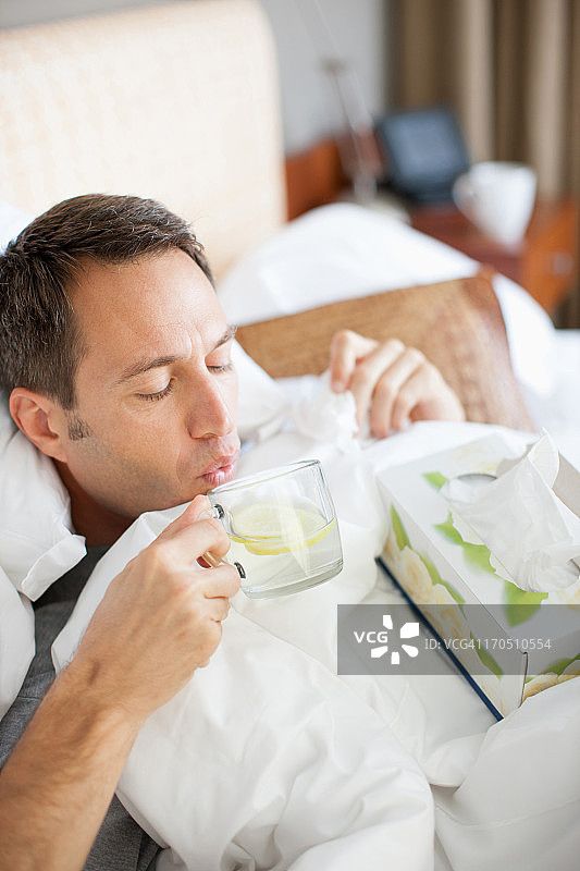 男人卧病在床，喝着热饮图片素材