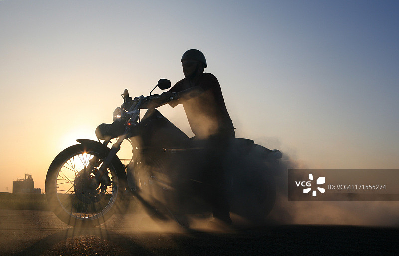 蓝色的草原天空衬托出冒烟的摩托车和骑手的轮廓图片素材