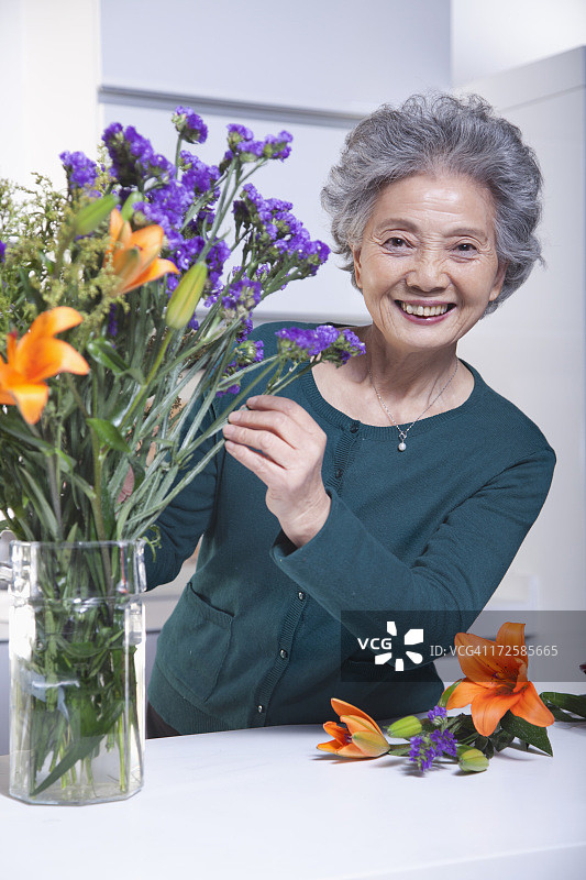 年长妇女触摸一束花在厨房，肖像图片素材