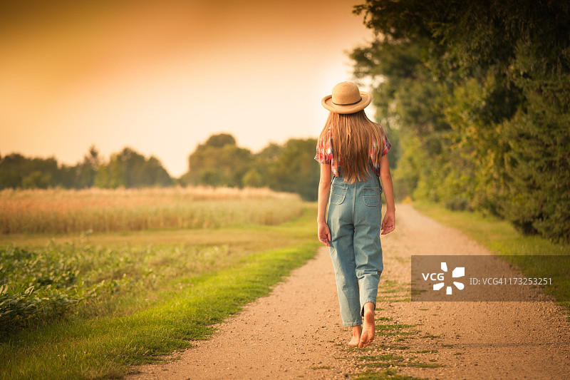 年轻的农家女孩走在田野边的乡间小路上图片素材