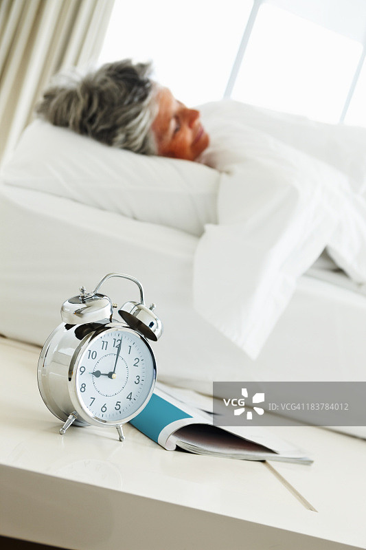 一位老妇人睡在旁边，她的闹钟就在旁边图片素材