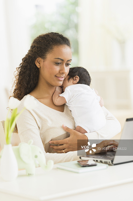 西班牙裔母亲抱着婴儿抱着笔记本电脑图片素材