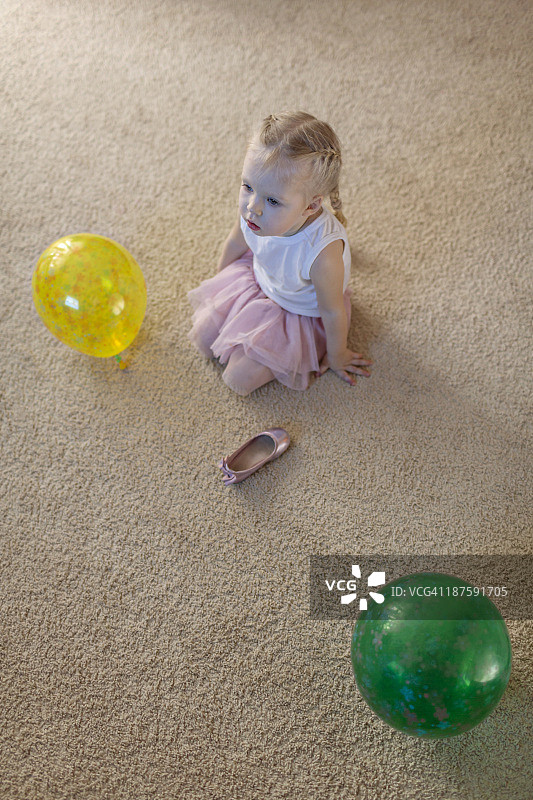 小女孩站在两个气球之间，她的芭蕾舞鞋躺在地板上图片素材