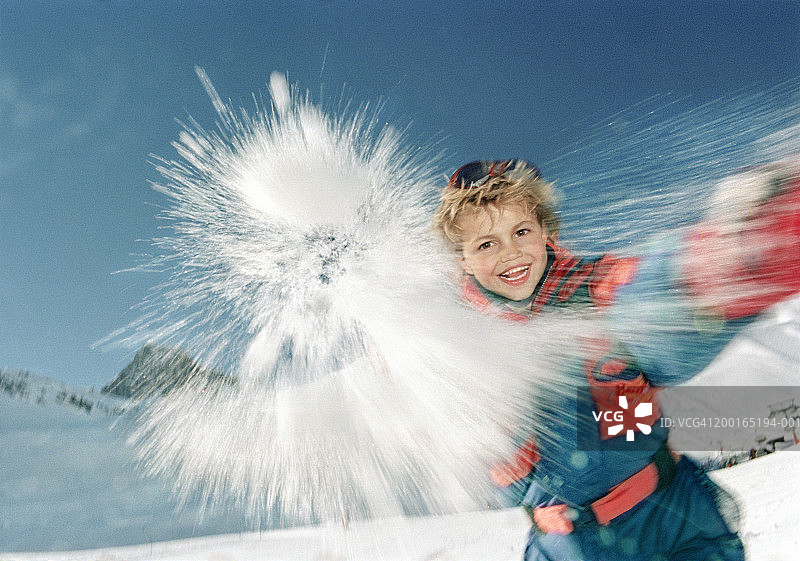 男孩(5-7)在户外雪地里，扔雪球，微笑着，画像图片素材