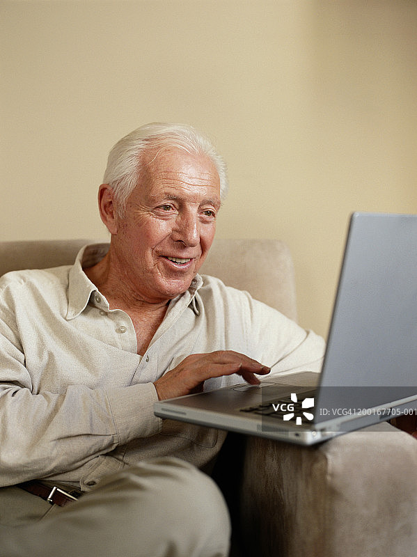 老人在沙发上用笔记本电脑，微笑着图片素材