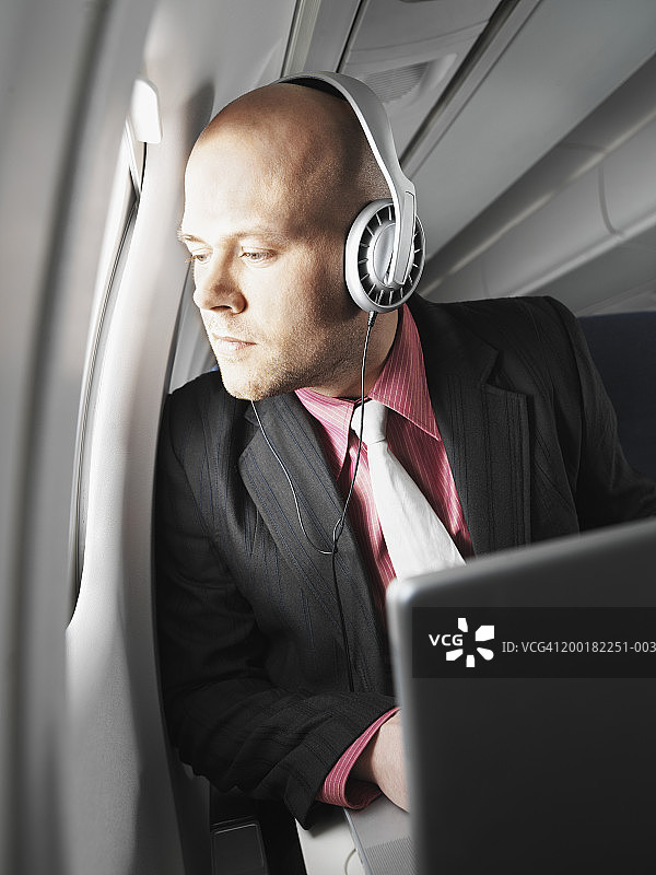 商人在飞机上，戴着耳机，看着窗外图片素材