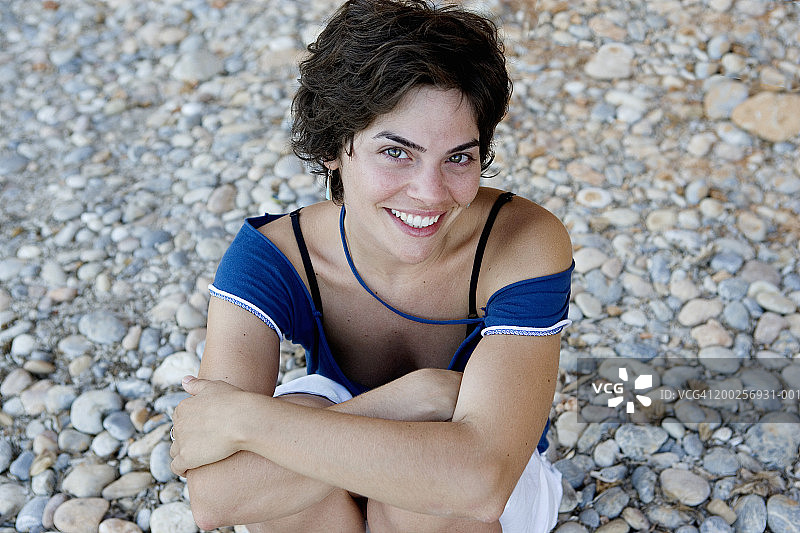 年轻女子坐在卵石滩上，微笑着，特写，肖像图片素材