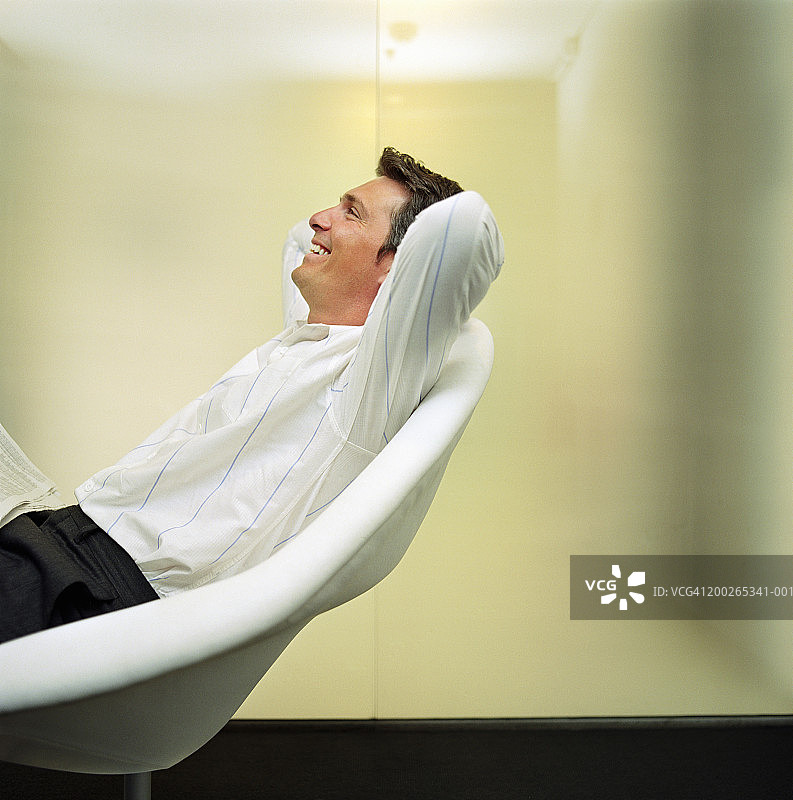 男人放松在椅子上，手臂放在脑后，侧视图片素材