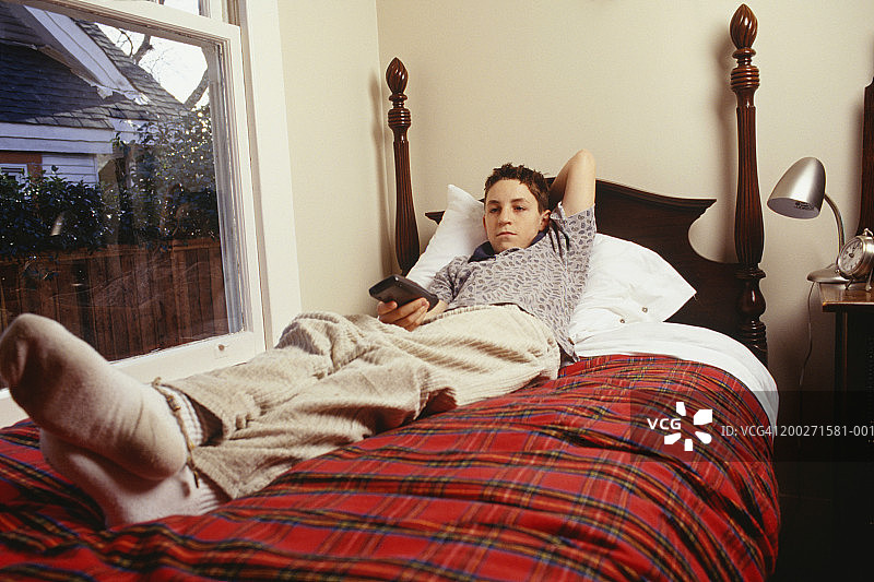 少年(16-17岁)拿着电视遥控器躺在床上图片素材