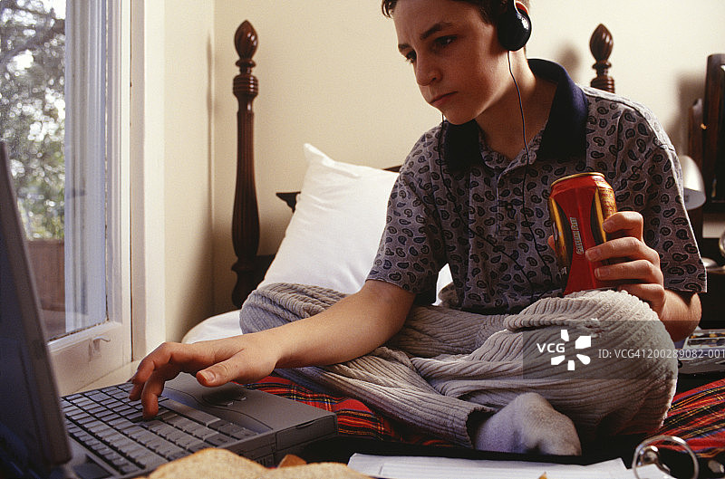 16-17岁的男孩坐在床上使用笔记本电脑图片素材