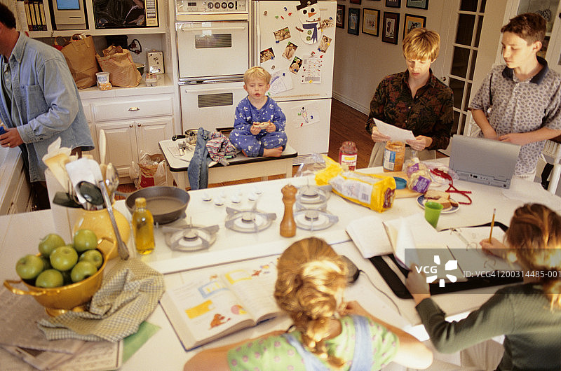 早上大家庭在厨房里，女儿们(8-9岁)在做作业，俯瞰高处图片素材