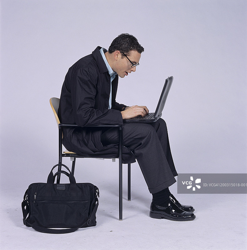 戴眼镜的商人坐着，使用笔记本电脑图片素材