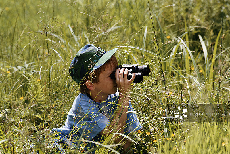 男孩(8-9)在草地上用望远镜看图片素材