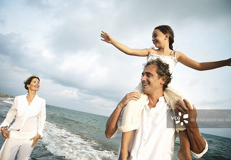 一对夫妇在海滩上，男人肩上扛着女儿(6-8岁)图片素材
