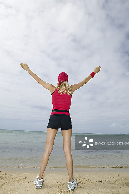 年轻女子站在沙滩上，伸开双臂，后视镜图片素材