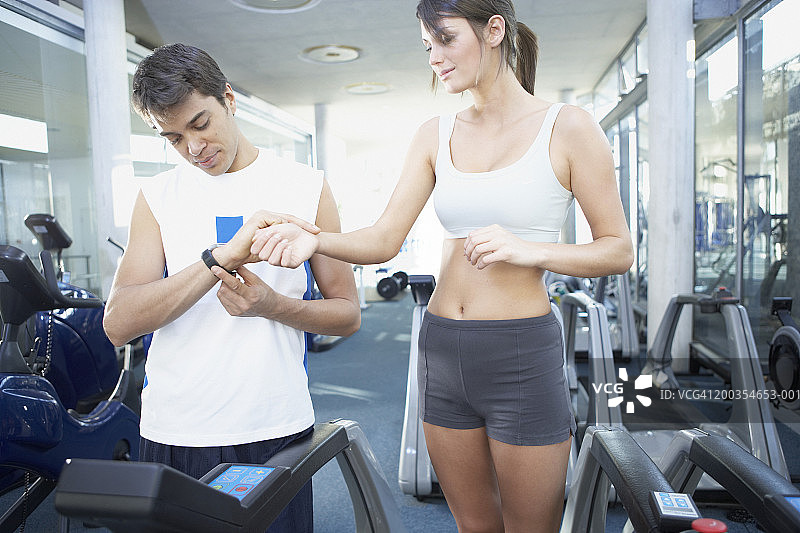 男人正在为站在跑步机上的年轻女子测脉搏图片素材