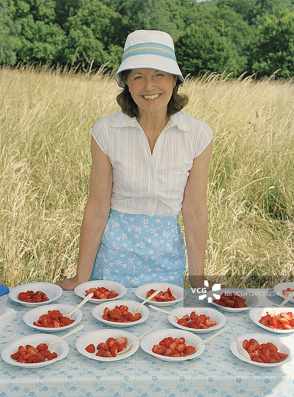 老妇人在户外捧着几碗草莓，面带微笑，画像图片素材