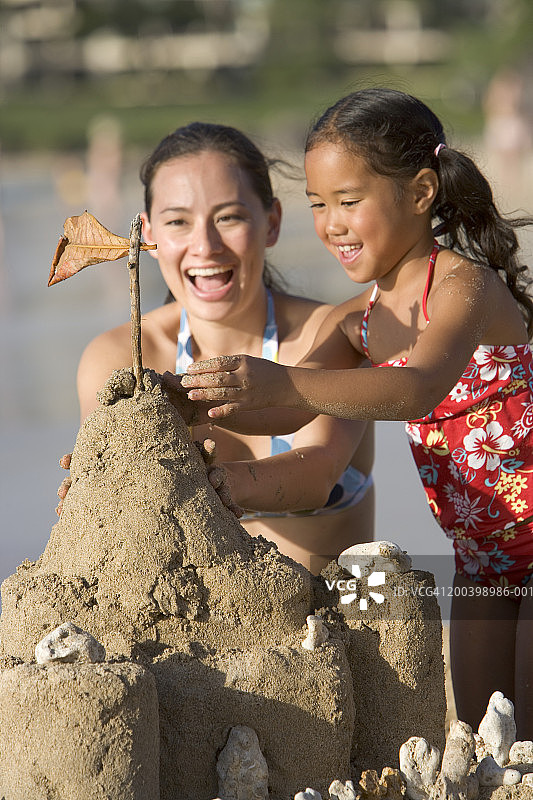母亲和女儿(5-7)建造沙堡，微笑着图片素材